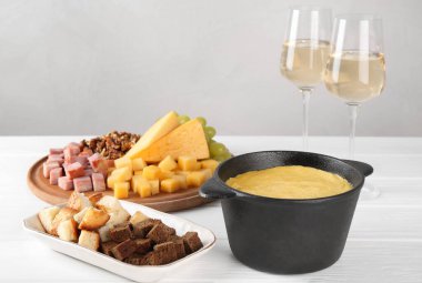 Lezzetli eritilmiş peynirli fondü, farklı ürünler ve beyaz ahşap masada bardakta aromatik şarap.