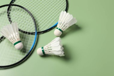 Yeşil arka planda badminton mekikleri ve raketler var. Metin için boşluk