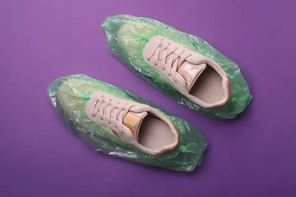 Sneakers in shoe covers on purple background, top view