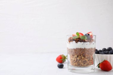 Böğürtlenli granola, yoğurt ve bardaktaki chia tohumları beyaz fayanslı masada, metin için yer var.