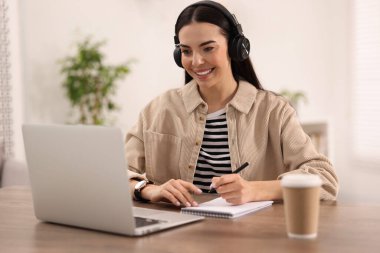 Kulaklıklı genç bir kadın masadaki Webinar 'ı izliyor.