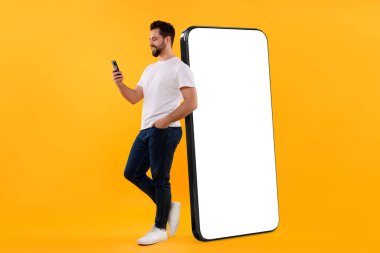 Cep telefonu olan bir adam koyu bej arka planda boş ekranlı büyük bir cihazın yanında duruyor. Tasarım için model
