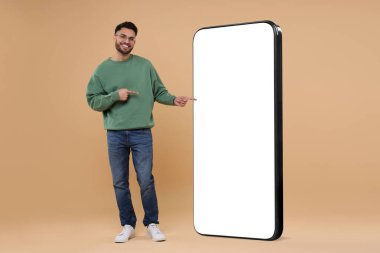 Koyu bej arka planda boş ekranı olan büyük bir cep telefonunu işaret eden bir adam. Tasarım için model