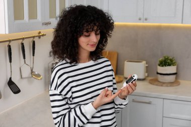 Diyabet. Mutfakta glukometreyle kan şekerini ölçen bir kadın var.