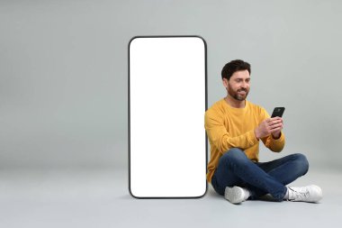 Cep telefonu olan bir adam gri arka planda boş ekranı olan büyük bir cihazın yanında oturuyor. Tasarım için model