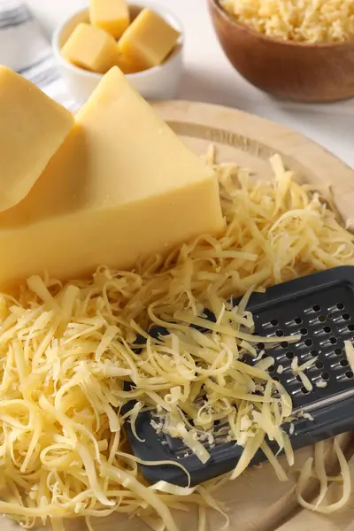 Grated, whole pieces of cheese and grater on table, closeup