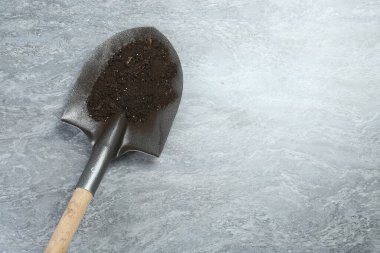 Gri desenli yüzeyinde verimli toprak bulunan metal kürek, üst manzara. Metin için boşluk