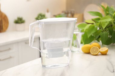Mutfaktaki beyaz mermer masada su filtresi, cam ve limon.