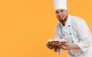 Sarı arka planda lezzetli kekler tutan üniformalı mutlu profesyonel pastacı. Metin için boşluk