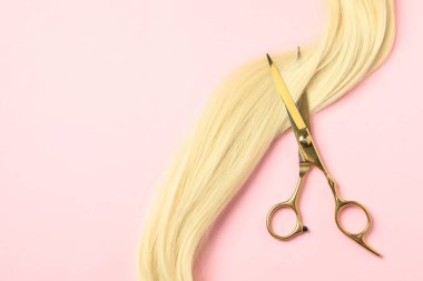 Pembe arka planda sarı saç teli olan profesyonel kuaför makası. Metin için boşluk