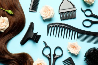 Açık mavi arka planda, profesyonel kuaför aletleri, çiçekler ve kahverengi saç teli ile düz konum