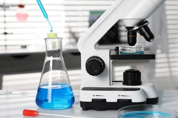实验室分析 将蓝色液体倒入靠近显微镜的白桌子上的瓶中 — 图库照片