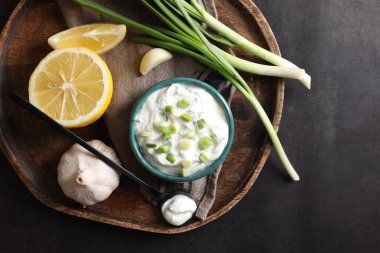 Lezzetli yoğurt kasede, yeşil soğan, sarımsak, limon ve kaşık siyah masada, düz yerde.