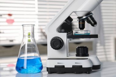 Laboratuvar analizi. Mavi sıvılı matara ve beyaz masada mikroskop