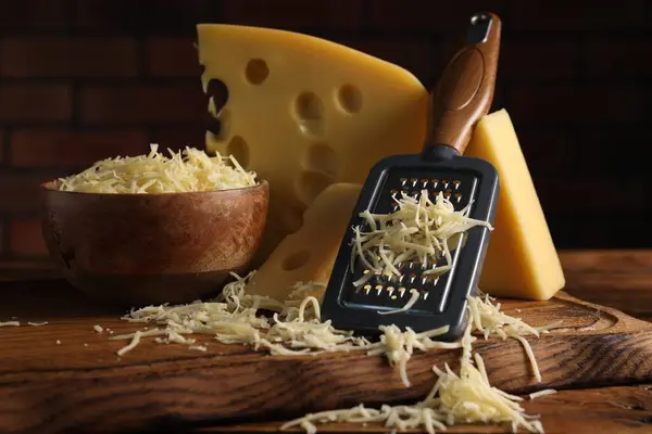 Grated, cut cheese and grater on wooden table, closeup