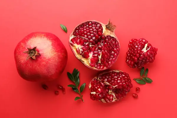 stock image Fresh pomegranates and green leaves on red background, flat lay