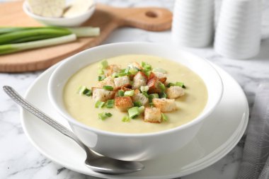 Lezzetli patates çorbası, kase içinde kızarmış ekmek ve beyaz mermer masada kaşık.