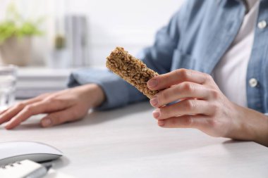 İçerideki aydınlık masada lezzetli granola barını tutan kadın, yakın plan.