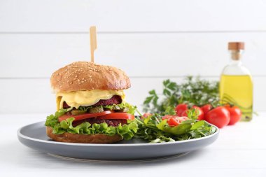 Beyaz ahşap masada salata ile servis edilen lezzetli vejetaryen burger.