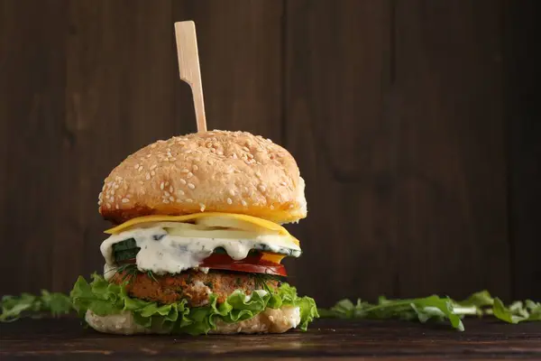 Delicious vegetarian burger and arugula on wooden table, space for text