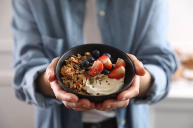 Elinde meyveli, yoğurtlu ve tohumlu bir kase lezzetli granola tutan kadın, yakın plan.