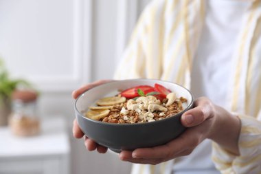 Elinde muzlu, kaju fıstıklı ve çilekli bir kase lezzetli granola tutan kadın, yakın plan.