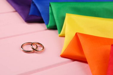 Gökkuşağı LGBT bayrağı ve alyanslar pembe ahşap masada, yakın plan.