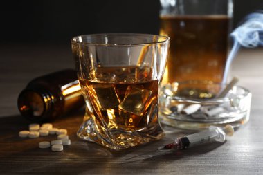 Alkol ve uyuşturucu bağımlılığı. Bardakta viski, şırınga, haplar ve sigaralar ahşap masada.