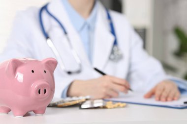 Doktor beyaz masada notlar alıyor, domuz kumbarasına odaklan.