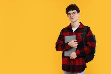 Sırt çantası, dizüstü bilgisayarı ve turuncu arka planda gözlüğü olan öğrenci portresi. Metin için boşluk