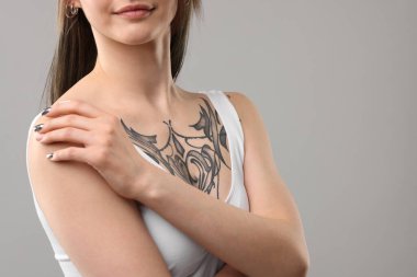 Gri arkaplanda havalı dövmeleri olan kadın, yakın plan.