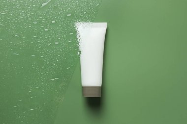 Islak yeşil yüzey üzerinde nemlendirici krem bulunan tüp, üst manzara.