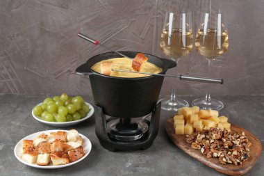 Lezzetli eritilmiş peynirli fondü tenceresi, çatal, şarap ve gri masada farklı atıştırmalıklar.