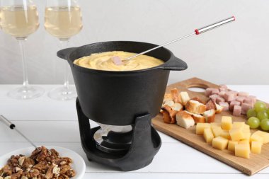 Lezzetli peynirli fondü tenceresi, çatal, şarap ve beyaz ahşap masada farklı atıştırmalıklar.