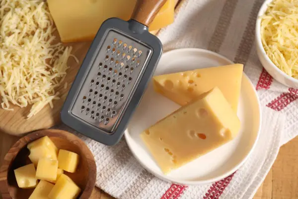 Grated, cut cheese and grater on wooden table, flat lay