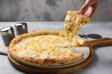 Açık gri masada lezzetli peynirli pizza yiyen bir kadın, yakın plan.