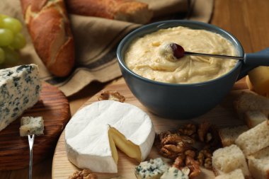 Lezzetli eritilmiş peynirli fondü tenceresi, çatal ve masada farklı atıştırmalıklar.