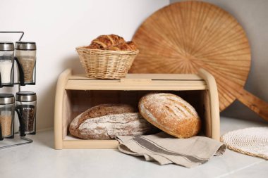 Tahta ekmek sepeti, taze pişmiş somunlar ve mutfaktaki beyaz mermer masada kruvasanlar.