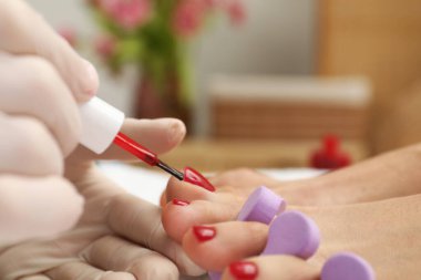 Güzellik salonunda pedikür uzmanının ayak tırnaklarına kırmızı oje sürmesi, yakın plan.