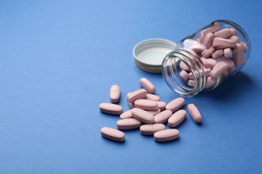 Mavi arkaplanda pembe vitamin kapsülleri, metin için boşluk