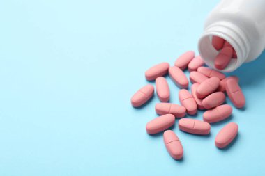 Açık mavi arka planda vitamin hapları ve şişe, yakın plan. Metin için boşluk