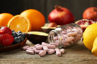 Şişede vitamin hapları ve tahta masada taze meyveler.