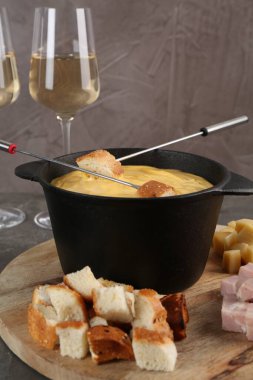 Lezzetli eritilmiş peynirli fondü tenceresi, çatal, şarap ve gri masada farklı atıştırmalıklar.