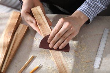 Gri masadaki zımpara kağıdıyla tahta cilalayan adam, yakın plan.