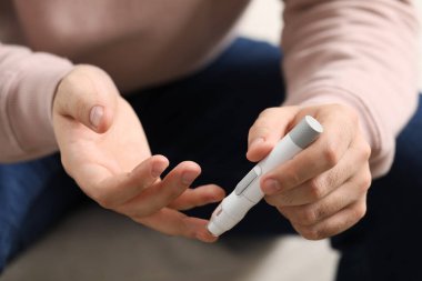 Diyabet testi. Bulanık arka planda kan şekeri seviyesini tükenmez kalemle ölçen adam, yakın plan.