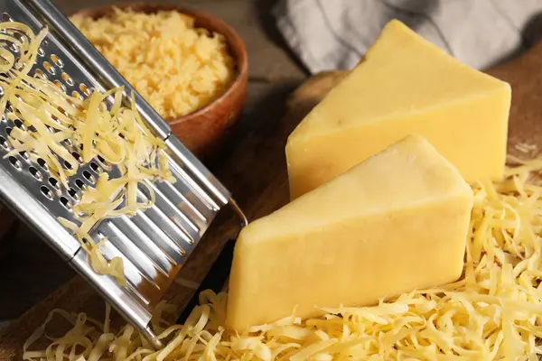Grated, whole pieces of cheese and grater on table, closeup