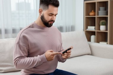 Diyabet testi. Evdeki koltukta kan şekerini tükenmez kalemle ölçen bir adam var.