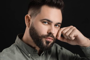 Siyah arka planda bıyıklı genç bir adam.