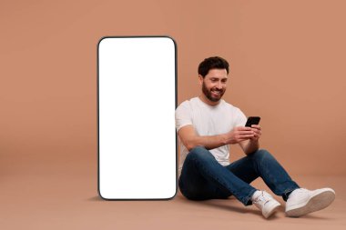 Cep telefonu olan bir adam koyu bej arka planda boş ekranı olan büyük bir cihazın yanında oturuyor. Tasarım için model