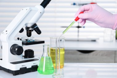 Laboratuvar analizi. Beyaz masada test tüpüne sıvı damlatan bir kadın, yakın plan.